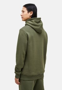 Oliegroene hoodie van zacht materiaal, met een grote capuchon, geribbelde manchetten en een losse pasvorm, ontworpen voor casual draag.