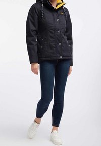 Svart jacka med ett gult innerfoder, som har knappar och två sidofickor. Kombineras med mörka jeans och vita sneakers.