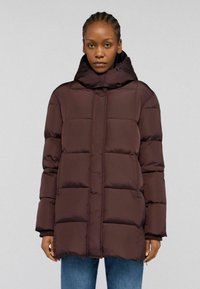Giubbotto a vento bordeaux con colletto alto, sezioni quadrate trapuntate, tasche frontali e una superficie liscia. Indossato sopra jeans blu.