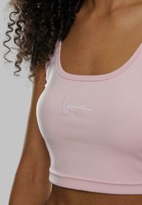Lyse rosa crop top laget av glatt stoff, med firkantet utringning og brodert logo i hvitt. Tettsittende passform med subtile sømdetaljer.
