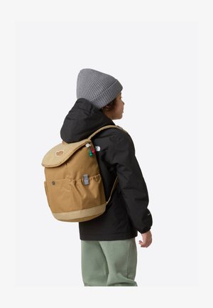 Bruine rugzak met een getextureerde beige klep, zijzak en groene accenten. Draagt door een kind in een zwart jasje en een grijze muts.