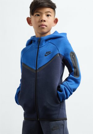 Sweat à capuche bleu et marine fabriqué en tissu doux. Doté d'une poche zippée sur le bras et d'accents noirs sur la fermeture éclair et les manches.