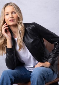 Black leather jacket with a fitted design, zip closure, and ribbed cuffs, worn over a white t-shirt and paired with blue jeans.