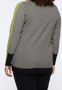 Knitted sweater with black and white herringbone pattern, green accent on the shoulder, rounded hem, and ribbed black cuffs and bottom.