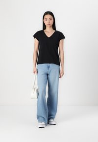 Svart V-ringad t-shirt med korta ärmar, kombinerad med ljusblå vida jeans, vita sneakers och en liten vit axelväska.