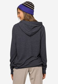 Mørkegrå hoodie med en løs pasform, der har en hætte og subtil tekstur, parret med en stribet blå og sort strikket hue.
