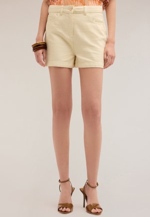 Shorts in cotone color crema con chiusura a pulsante, tasche frontali e vita piatta. Abbinati a sandali alti con cinturini marroni.
