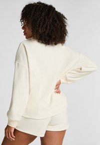Crème-kleurig fleece sweatshirt met een lage schouderlijn en geribde manchetten, gecombineerd met bijpassende shorts, heeft een gladde textuur en een ontspannen pasvorm.