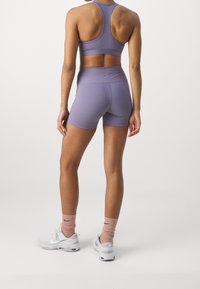 Bra sportivo viola e pantaloni corti realizzati in tessuto elastico. Scarpe da ginnastica bianche con calzini rosa. Incentrato su vestibilità e design funzionale.