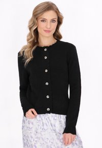 Černý pletený cardigan s kulatým výstřihem, pěti stříbrnými knoflíky a žebrovanými manžetami, nošený přes sukni s květinovým vzorem.