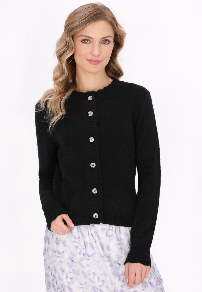 Černý pletený cardigan s kulatým výstřihem, pěti stříbrnými knoflíky a žebrovanými manžetami, nošený přes sukni s květinovým vzorem.