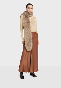 Bež bluzica dugih rukava, svijetlosmeđi krzneni šal i smeđa saten suknja s bočnim prorezima. Crne čizme s potpeticama do članaka upotpunjuju outfit.