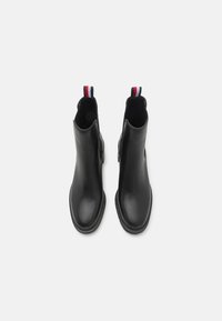Paire de bottines noires élégantes à bouts ronds avec des languettes à rayures rouge, blanc et bleu sur un fond blanc.