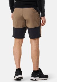 Pantaloni corti realizzati in tessuto marrone e nero con un design bicolore. Presentano cerniere sui lati e una finitura testurizzata. Indossati con scarpe sportive nere.
