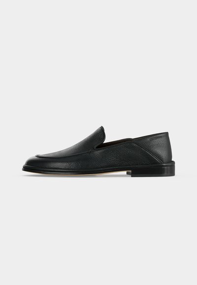 Mocassin en cuir noir sans lacets avec petit talon et bout arrondi, présenté sur un fond blanc uni.