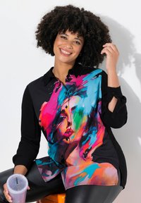 Kleurzaam button-up shirt met een levendig, abstract portret en zwarte mouwen. Zachte stof en glanzende afwerking, gecombineerd met leggings.