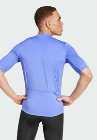 Maglietta sportiva da uomo in tessuto blu chiaro. Presenta maniche corte, una silhouette aderente e una tasca con zip sul retro con una striscia riflettente.