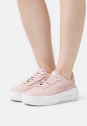 Sneakers in pelle rosa chiaro con suola in gomma bianca, caratterizzate da perforazioni, punta arrotondata e dettagli testurizzati. Lacci e marchio visibili.