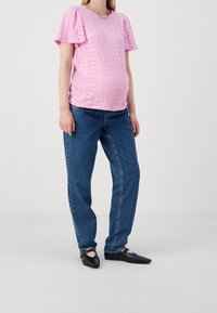 Różowa bluzka z ażurowymi wycięciami i krótkimi puff-sleeves, zestawiona z niebieskimi jeansami o luźnym kroju i czarnymi płaskimi butami. Bluzka prezentuje teksturowany wzór.