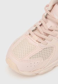 Világos rózsaszín sportcipő hálós betétekkel, párnázott nyelvvel és kerek fűzőkkel. Mintázott gumitalppal és varrás részletekkel rendelkezik.