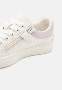 Hvit sneakers med lilla accenter, teksturert lær, rundt nese og snøring. Sidelommer med glidelås og gummisåle.