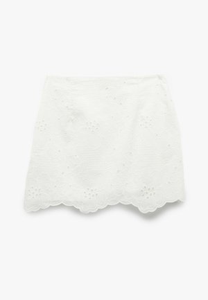 Weißer Blumen-Spitzen-Minirock mit welligem Saum, der bestickte Blumen und Ausschnittdetails auf einem strukturierten Stoff zeigt.
