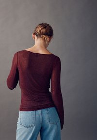 Dugotrajna uska majica tamnocrvene boje s teksturiranim materijalom, s okruglim izrezom. Kombinirana s trapericama svijetloplavih visokog struka.