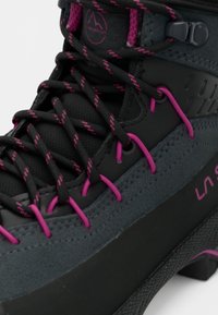 Botas de caminhada pretas e cinzas com detalhes em rosa e materiais texturizados, apresentando um cordão intrincado e uma sola em borracha para tração.