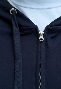 Marineblauwe rits hoodie met een zilverkleurige rits, voorzien van een zachte textuur en een contrasterende lichtblauwe binnenlaag, met koordjes en metalen accenten.