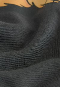 Fekete szövet texturált szövési mintával, redőkkel és gyűrődésekkel. Az anyag puhanak tűnik, részletesen látható a textúra közelről.