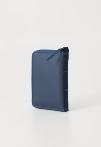 Pochette rectangulaire compacte zippée de couleur bleu marine avec un onglet en tissu, se tenant debout sur une surface blanche.