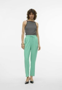 Zwart-wit gestreepte tanktop gecombineerd met mintgroene tapered broek. De broek heeft een elastische tailleband en een trekkoord. Zwarte hakken.