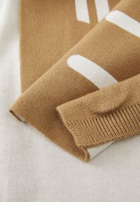 Tessuto di maglione lavorato a maglia in beige e marrone con ampie strisce bianche. Lana testurizzata con una finitura liscia; bordo leggermente arrotolato.