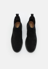 Schwarze Wildleder-Ankle Boots mit glatter Textur, elastischen Seitenpanelen und flachen Gummisohlen, die ein niedrig geschnittenes Design und Schlupfbänder aufweisen.