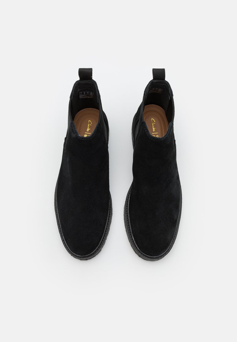 Bottines en suédine noire avec une texture lisse, des panneaux latéraux élastiques et des semelles en caoutchouc plates, présentant un design à coupe basse et des languettes de traction.