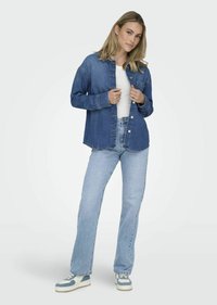 Jeansjack in medium blauw, met een knoopsluiting aan de voorkant en een zak. Gecombineerd met lichtblauwe recht-toe-recht-aan jeans en blauwe sneakers.