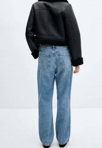 Giacca corta in similpelle nera con colletto in shearling, abbinata a jeans a gamba larga azzurri con tasche posteriori e texture slavata.