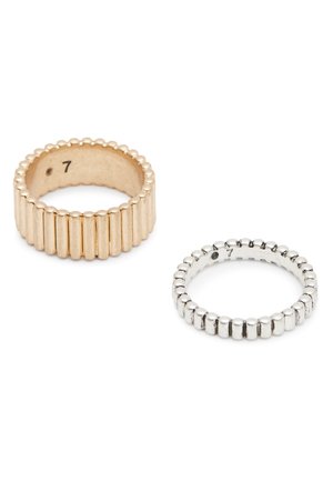 Zwei strukturierte Ringe, ein goldener und ein silberner, beide mit vertikalen Rillen und der Markierung Größe 7 innen, auf weißem Hintergrund.