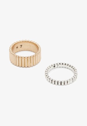 Dos anillos texturizados, uno de oro y otro de plata, ambos con estrías verticales y marcaciones de talla 7 en el interior, sobre un fondo blanco.