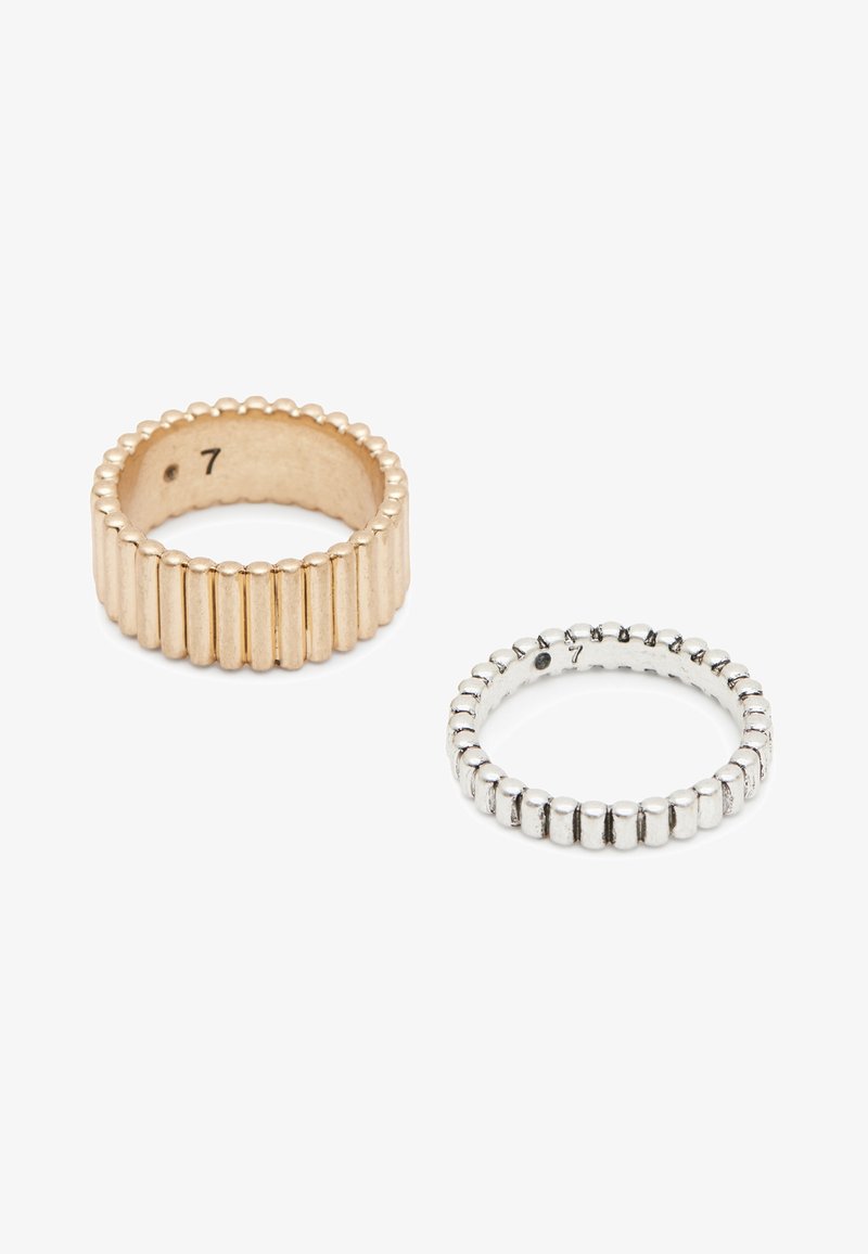 Deux bagues texturées, une en or et une en argent, toutes deux avec des rainures verticales et des marques de taille 7 à l'intérieur, sur fond blanc.