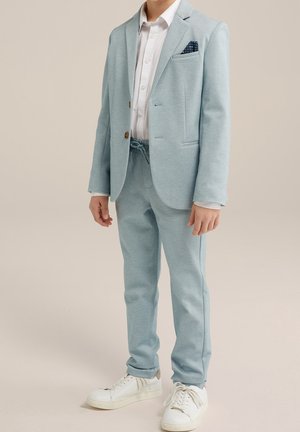 Jasnoniebieski garnitur z dopasowaną marynarką i pasującymi spodniami, biała koszula oraz granatowa poszetka. Noszony z białymi trampkami.