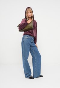 Bordeauxvelours hoodie met een trekkoord, losse lichtblauwe jeans en een groene handtas. Zwarte platte schoenen maken de outfit compleet.