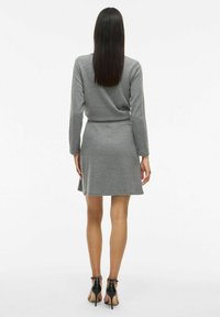 Robe en jersey gris avec des manches longues, un corsage ajusté et une jupe évasée. Texture lisse avec des détails côtelés. Portée avec des chaussures à talons hauts noires.