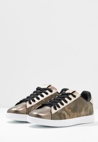 Brązowe trampki w kamuflażu z metalicznymi akcentami, czarnymi sznurówkami, białą gumową podeszwą oraz fakturowaną zamszową i skórzaną cholewką. Zaokrąglony nos.