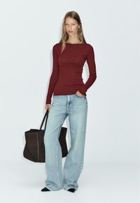 Long-sleeve burgundy and black striped top, light blue high-waisted wide-leg jeans, and a dark tote bag. The jeans have a frayed hem.