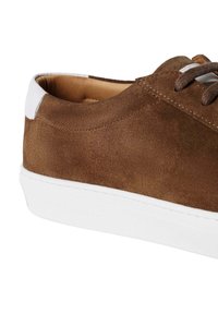 Sneakers en suède marron avec semelle en caoutchouc blanc et languette arrière. Présente des lacets ronds et une doublure intérieure lisse. Design minimaliste et détails de couture.