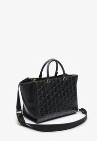 Borsa a tracolla in pelle nera con motivo geometrico in rilievo, doppi manici e tracolla regolabile con dettagli in metallo dorato.