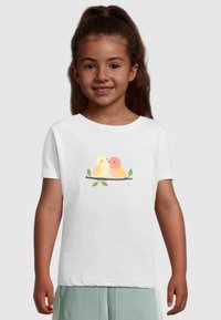 Witte t-shirt met korte mouwen, met een afbeelding van twee cartoonvogels die op een tak met bladeren zitten, in gele en oranje tinten.