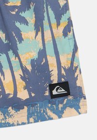 Šortyi z vzorcem palm, v modri, rumeni in teal barvi, z črnim logotipom s belim dizajnom na robu.