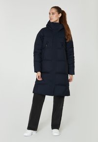 Abrigo acolchado de color navy con cuello alto, dos bolsillos frontales con cremallera y un diseño hasta la rodilla. La tela parece suave con una textura acolchada.